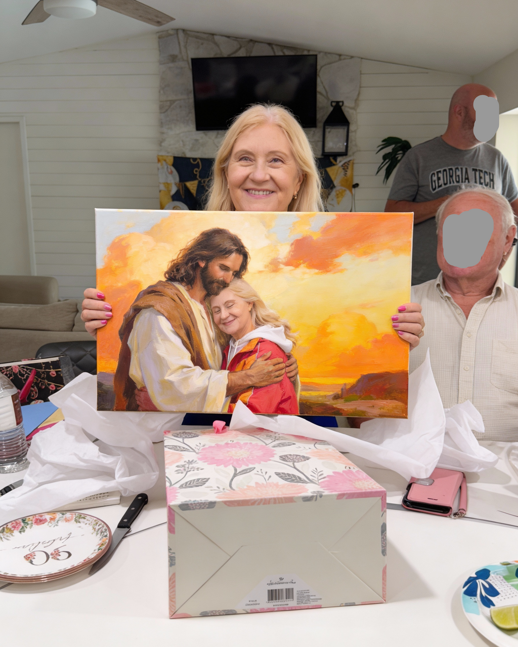 Woman holding her custom portrait  painting of a religious scene with two people, surrounded by family members in a home setting.